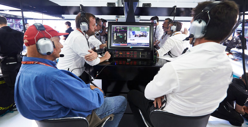 Un team di ingegneri e strateghi di Formula 1 controlla intensamente i dati di gara in diretta e i feed video sugli schermi dei computer del centro di comando della squadra durante un Gran Premio.