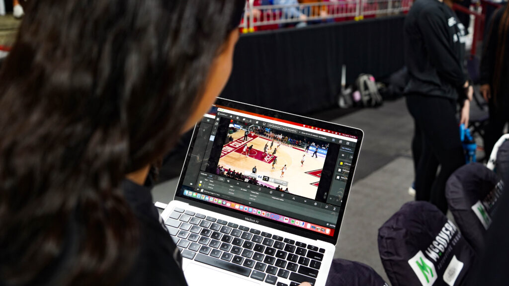 Se produce una interacción focalizada entre un jugador de baloncesto del Boston College y un entrenador, con el análisis de Pro Video Focus visible en la pantalla del portátil. Esto pone de relieve la integración del análisis de vídeo en directo en su entrenamiento, crucial para mejorar el rendimiento y las tácticas en el juego.